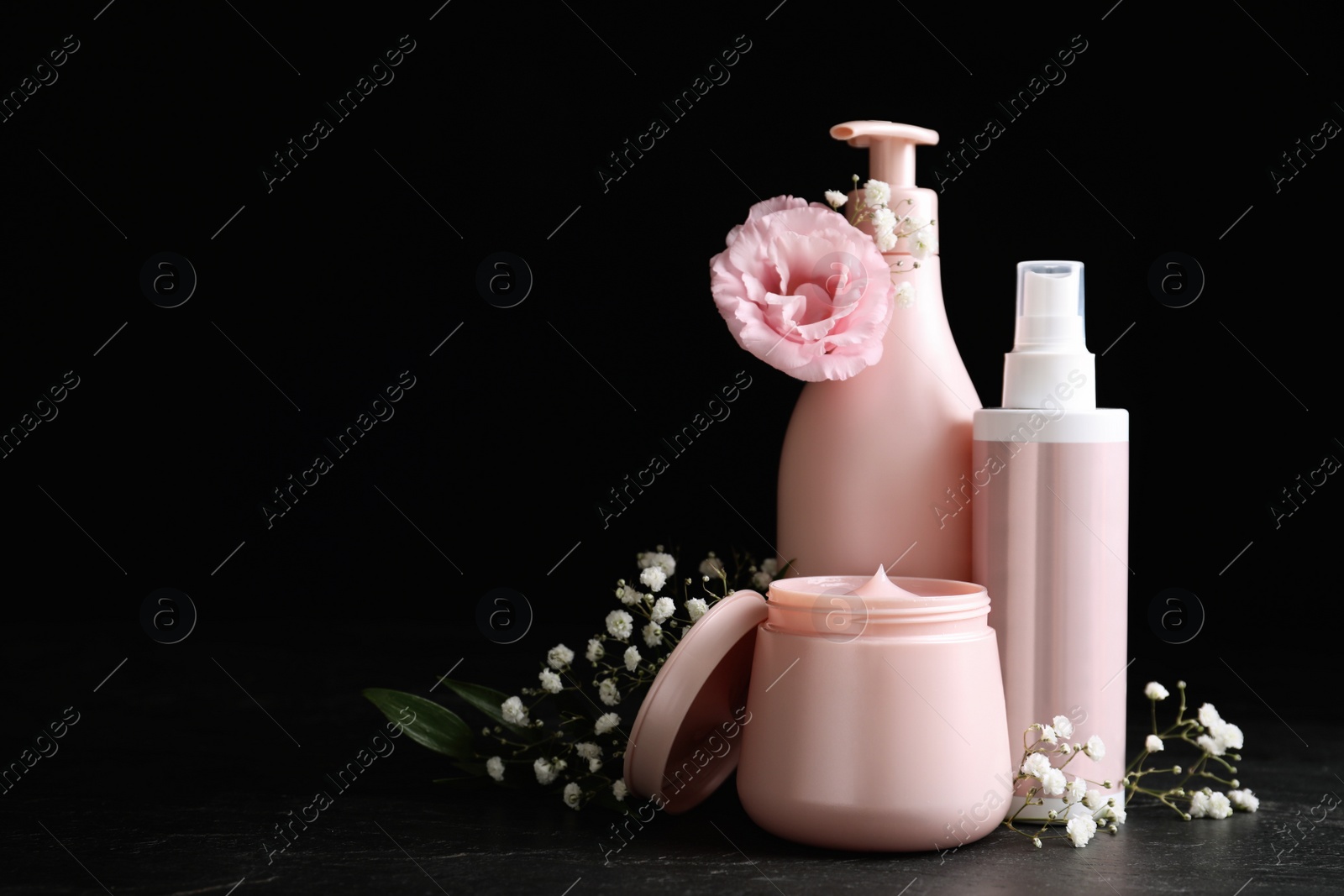 Photo of Set of hair cosmetic products and flowers on stone table against black background. Space for text