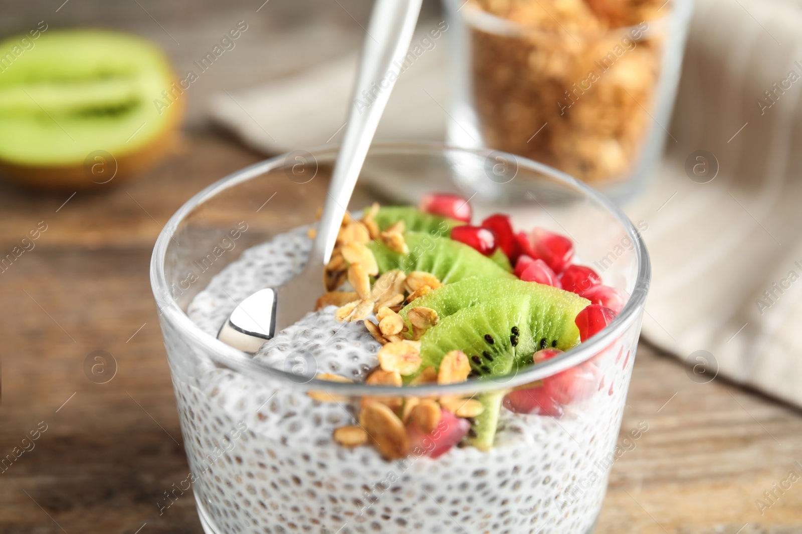 Photo of Dessert bowl of tasty chia seed pudding with granola, kiwi and pomegranate on table, closeup