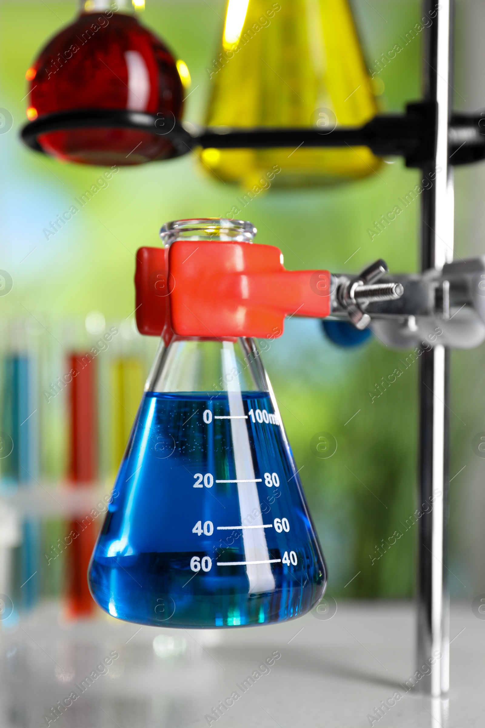 Photo of Retort stand and laboratory flasks with liquids on table against blurred background, closeup