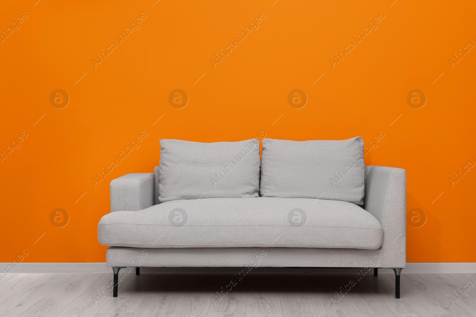 Photo of Comfortable sofa near bright orange wall indoors