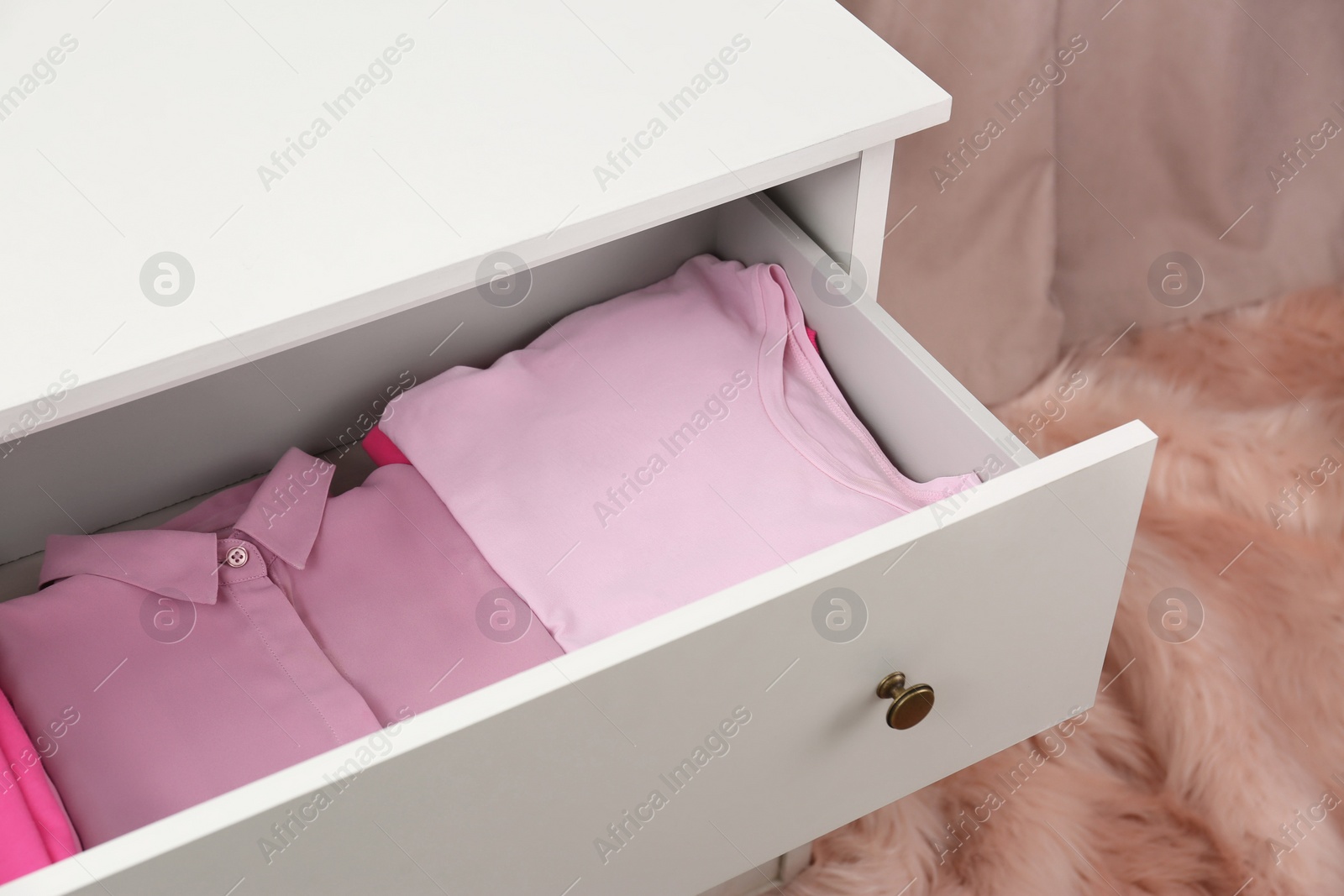 Photo of Many folded pink clothes in white chest of drawers indoors, closeup