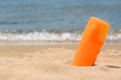 Photo of Bottle with sun protection spray on sandy beach near sea, space for text