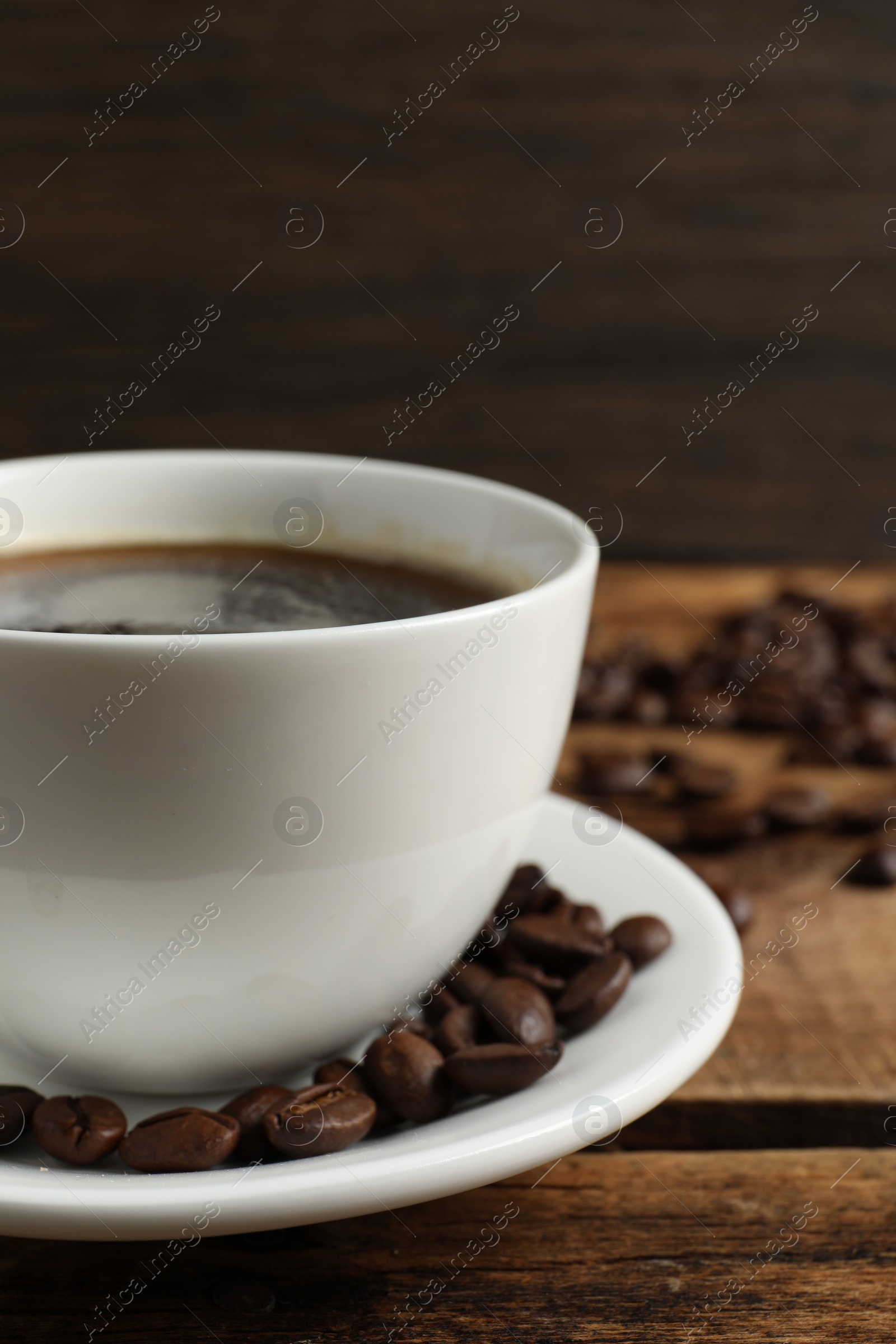 Photo of Cup of aromatic coffee and beans on wooden table, closeup. Space for text