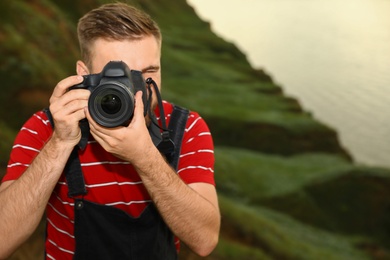 Male photographer taking picture with professional camera on green hill