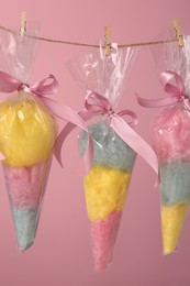 Packaged sweet cotton candies hanging on clothesline against pink background