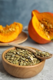 Photo of Bowl and spoon of raw pumpkin seeds on light grey marble table. Space for text