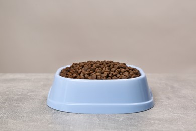 Photo of Dry food in light blue pet bowl on grey surface
