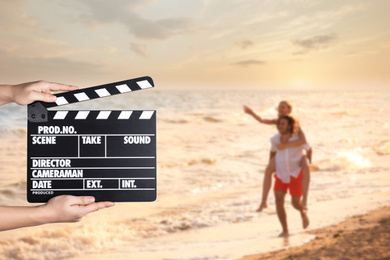Image of Assistant holding clapperboard and people having fun on beach at sunset, closeup. Cinema production