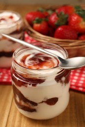 Photo of Tasty yoghurt with jam and strawberries on wooden table, closeup