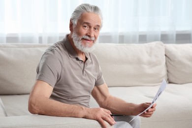 Photo of Senior man solving crossword on sofa at home