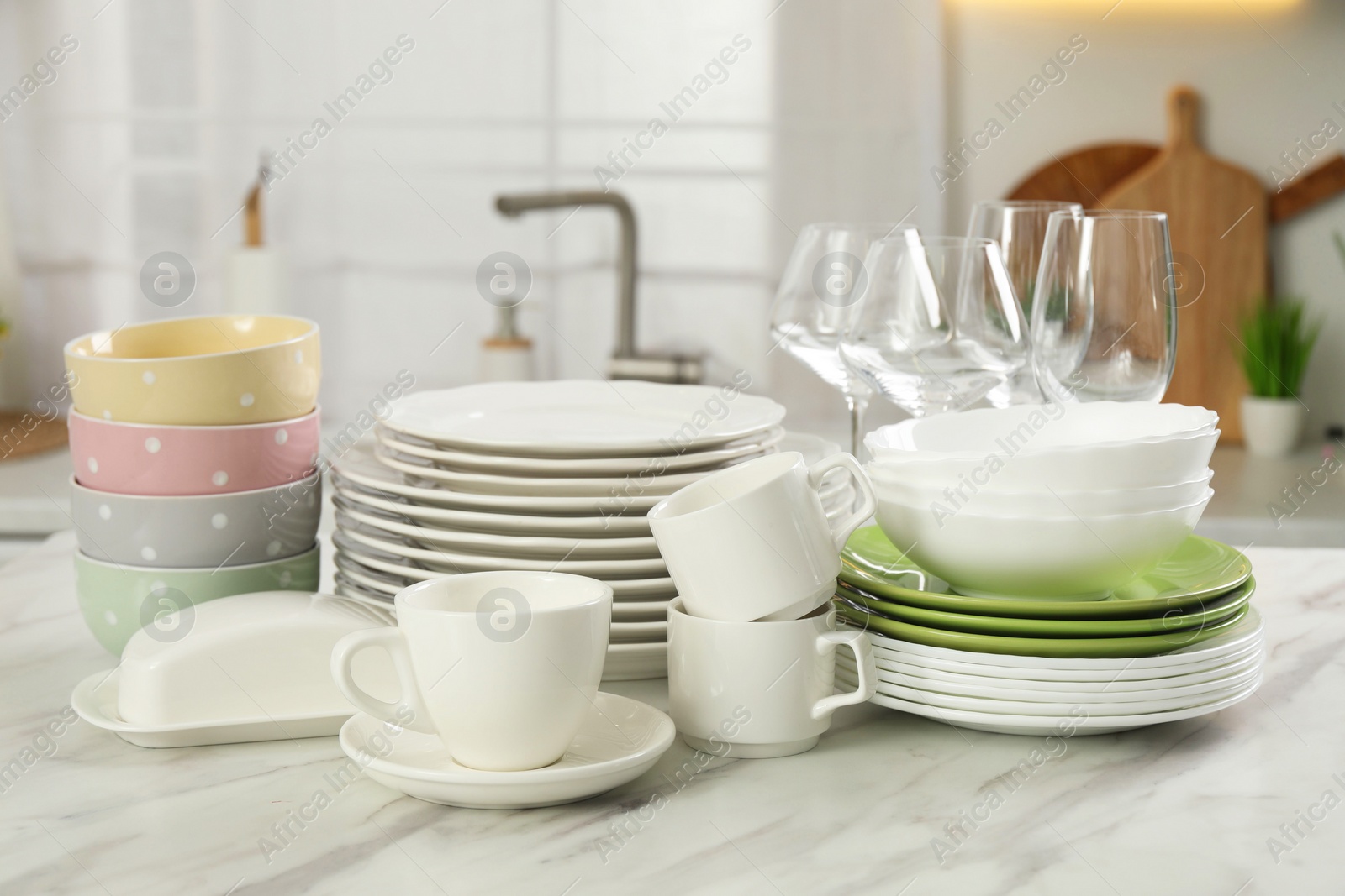 Photo of Clean plates, bowls, cups and glasses on white marble table in kitchen