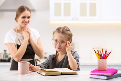 Photo of Happy mother watching her daughter doing homework in kitchen
