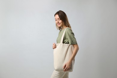 Photo of Happy young woman with blank eco friendly bag on light background