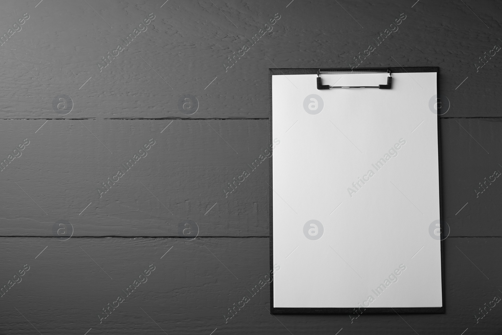 Photo of Clipboard with sheet of paper on black wooden table, top view. Space for text