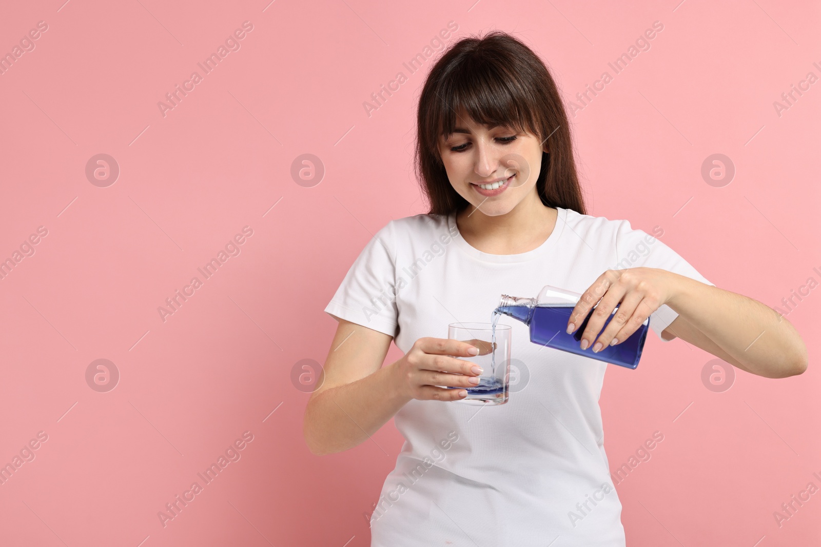 Photo of Young woman using mouthwash on pink background, space for text