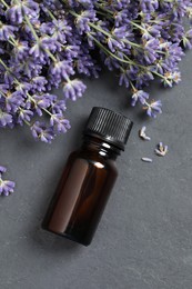 Bottle with essential oil near lavender on grey textured table, flat lay