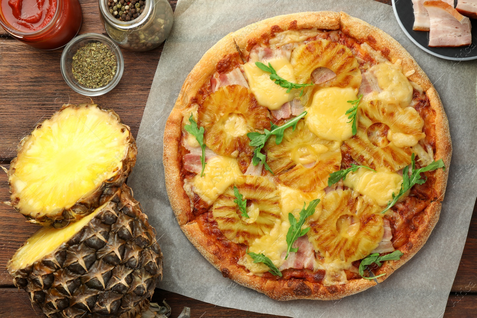 Photo of Delicious pineapple pizza and ingredients on wooden table, flat lay