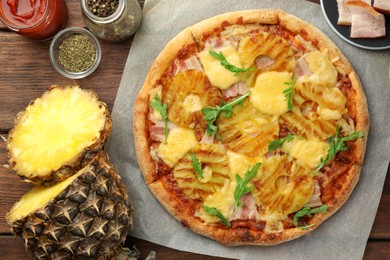 Delicious pineapple pizza and ingredients on wooden table, flat lay