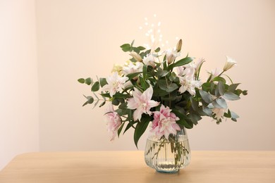 Photo of Bouquet of beautiful lily flowers in vase on wooden table against beige background