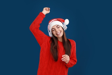 Young woman in Santa hat listening to Christmas music on dark blue background