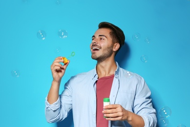 Photo of Young man blowing soap bubbles on color background