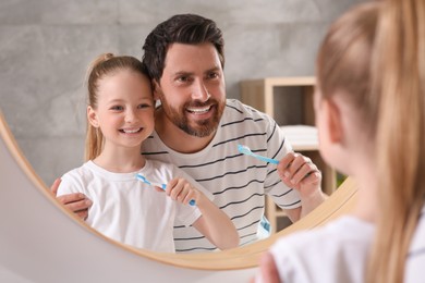 Photo of Father and his daughter brushing teeth together near mirror in bathroom