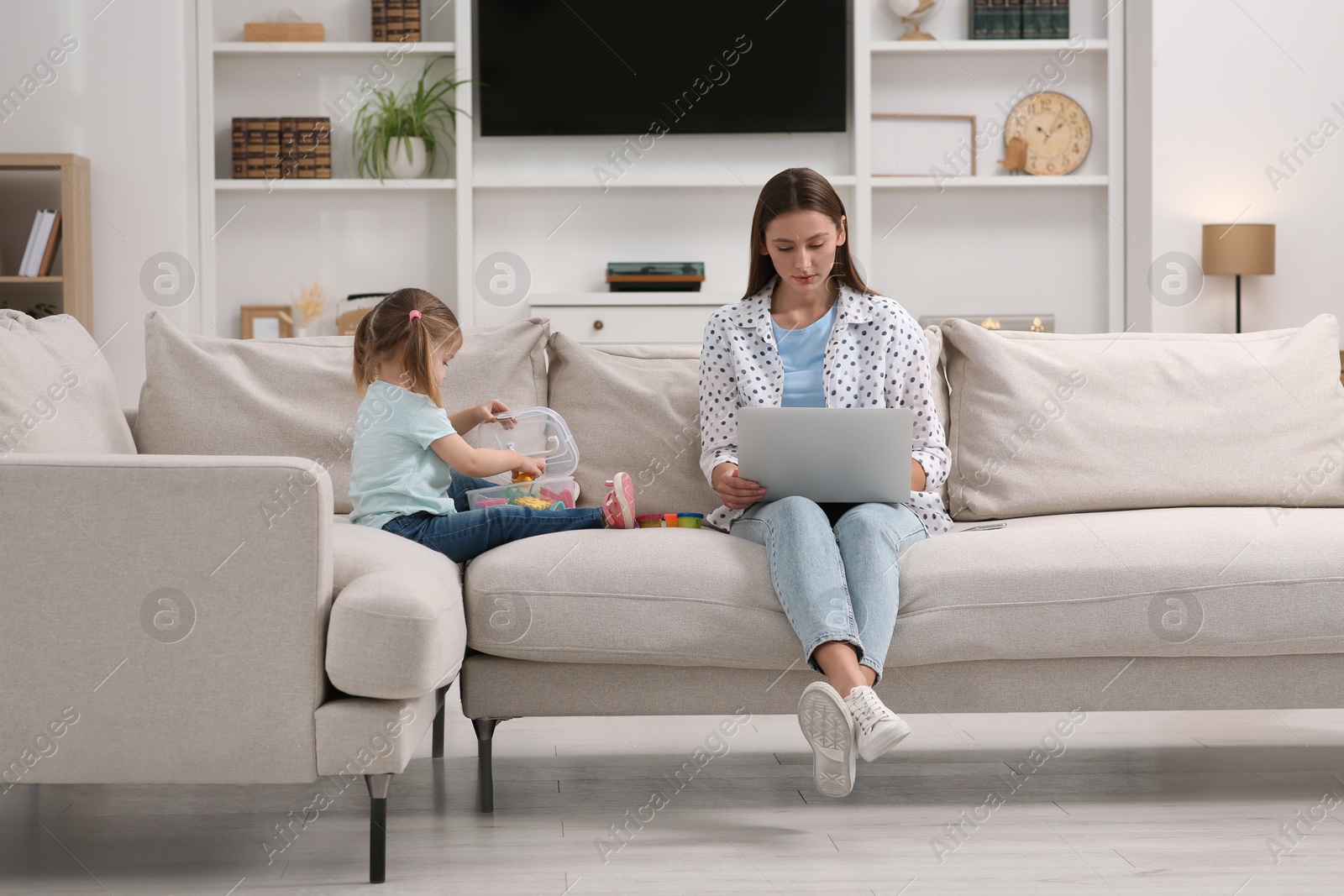 Photo of Little daughter playing while her mother working remotely on sofa at home