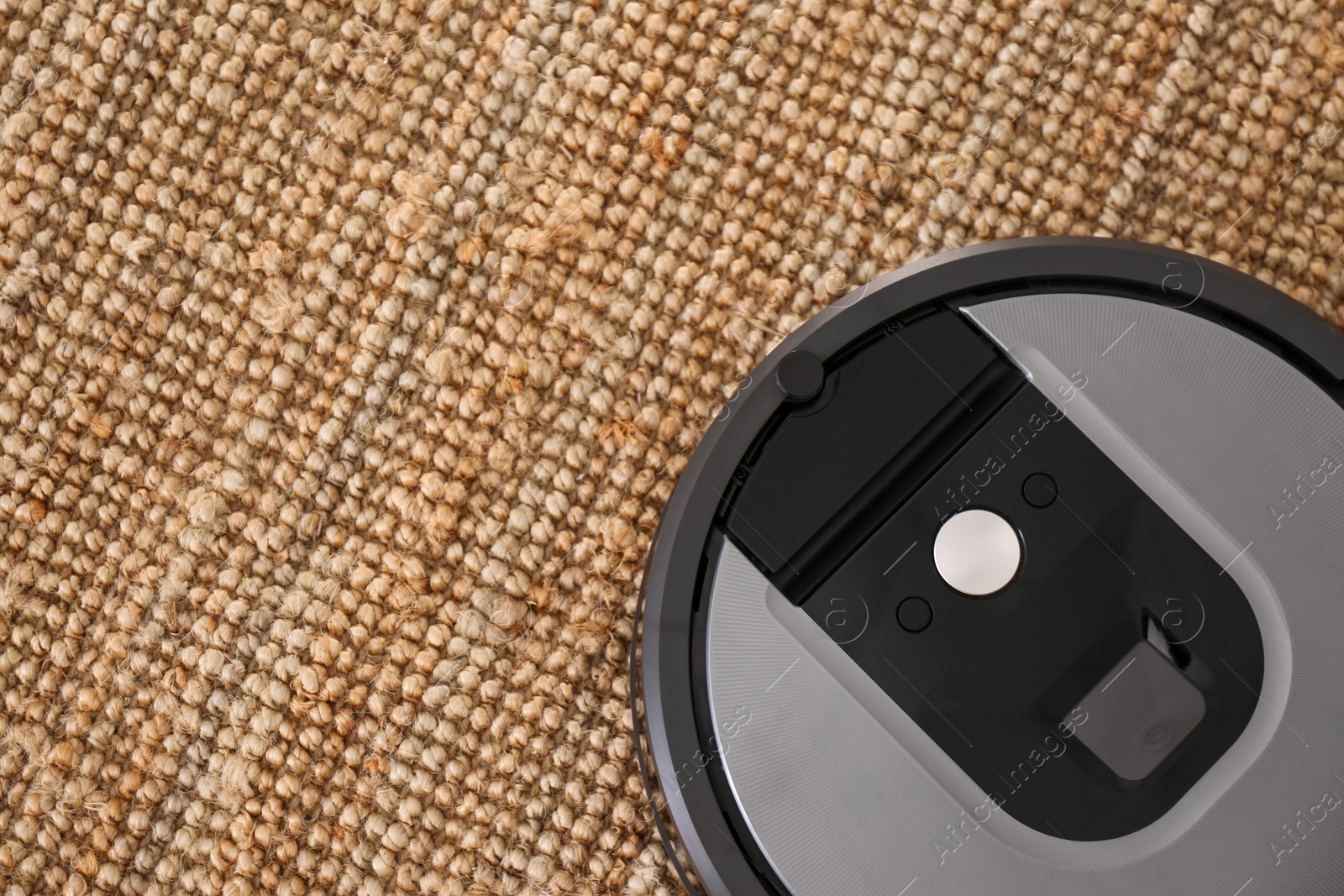 Photo of Modern robotic vacuum cleaner on brown rug, top view. Space for text
