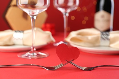 Photo of Joined forks with paper heart on red table, closeup. Romantic dinner