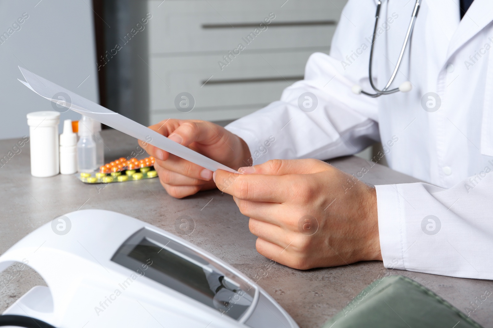 Photo of Doctor with papers and digital pressure meter at table, closeup. Medical objects