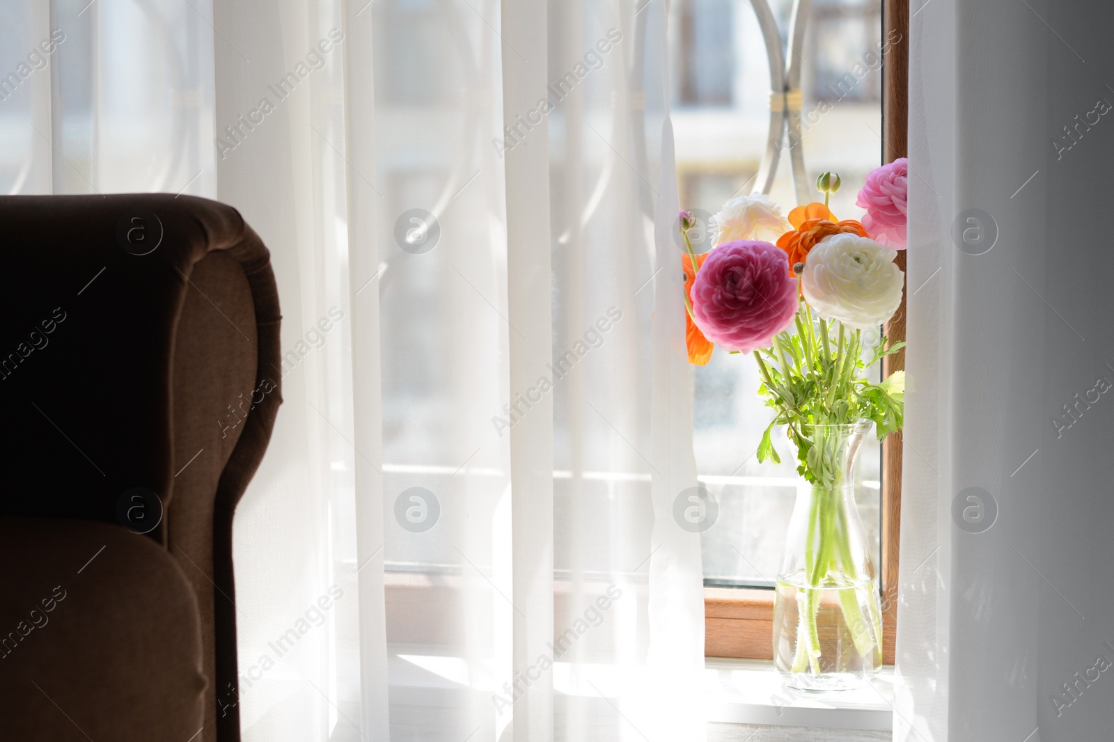 Photo of Bouquet of beautiful bright ranunculus flowers in glass vase on windowsill