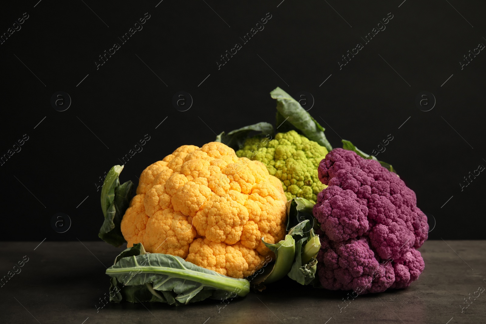 Photo of Colorful cauliflower cabbages on table against black background. Healthy food