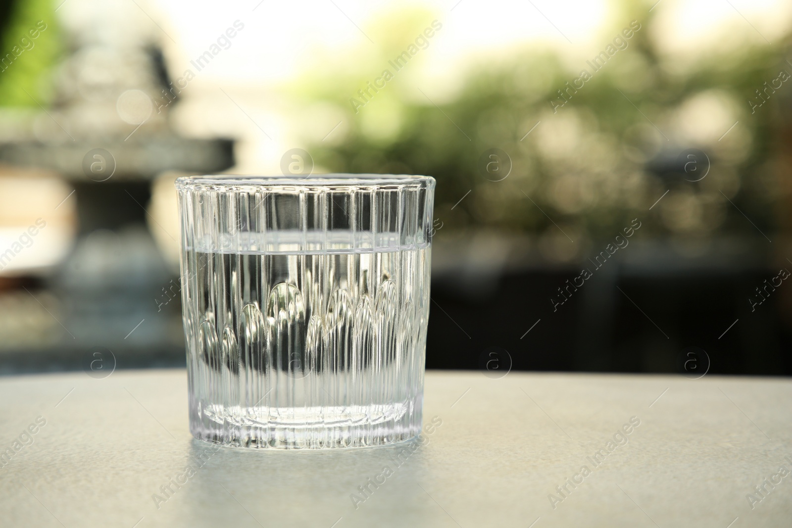 Photo of Glass of fresh water on light grey table outdoors, closeup. Space for text