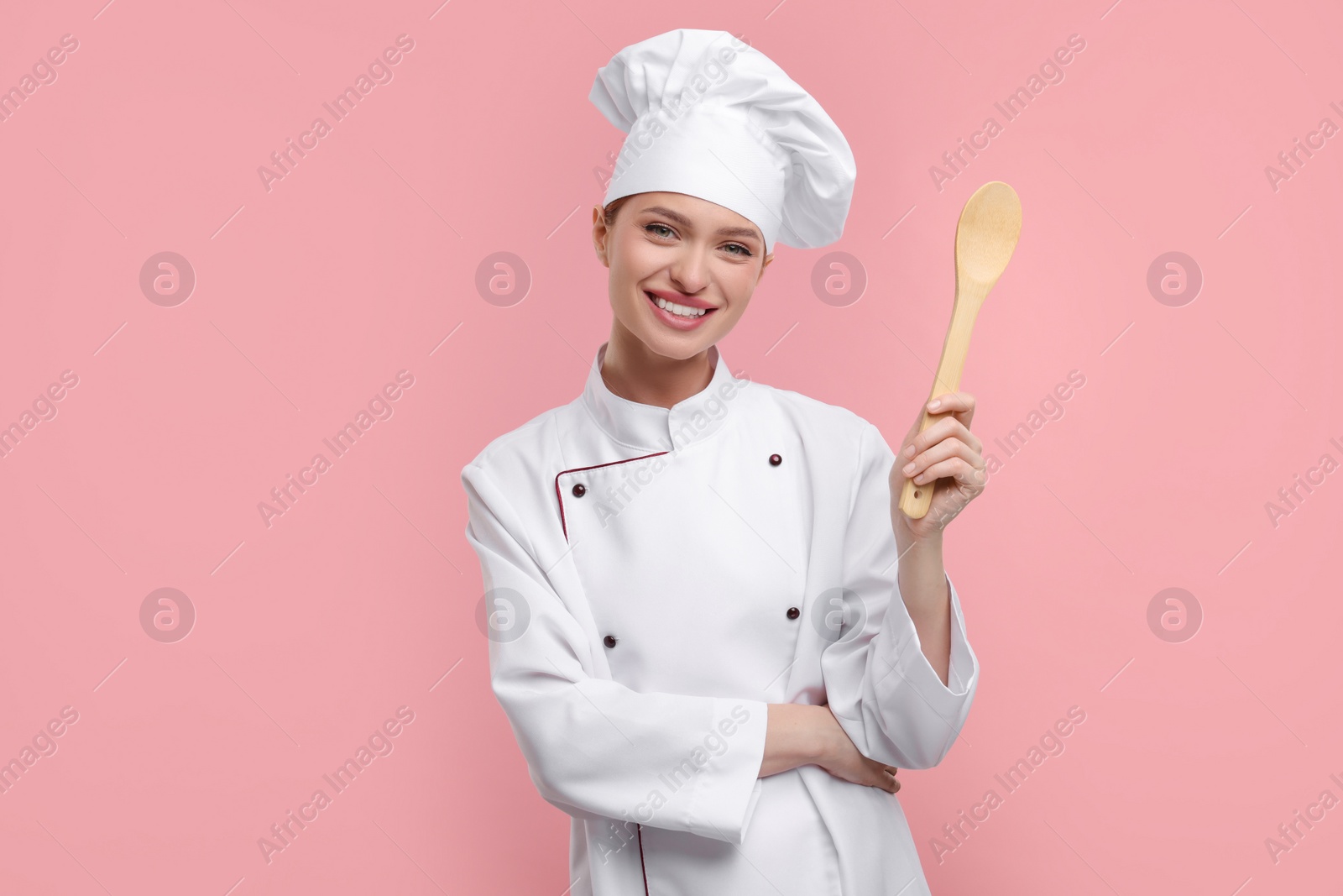 Photo of Happy chef in uniform holding wooden spoon on pink background
