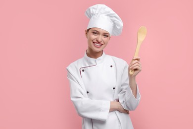 Photo of Happy chef in uniform holding wooden spoon on pink background