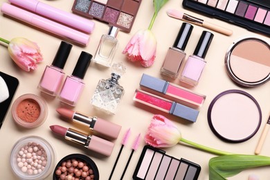 Photo of Flat lay composition with different makeup products and beautiful spring flowers on beige background