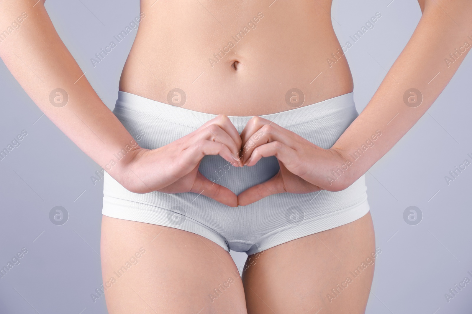 Photo of Young woman making heart symbol with hands near underwear on grey background. Gynecology