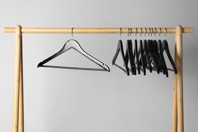 Photo of Black clothes hangers on wooden rack against light grey background