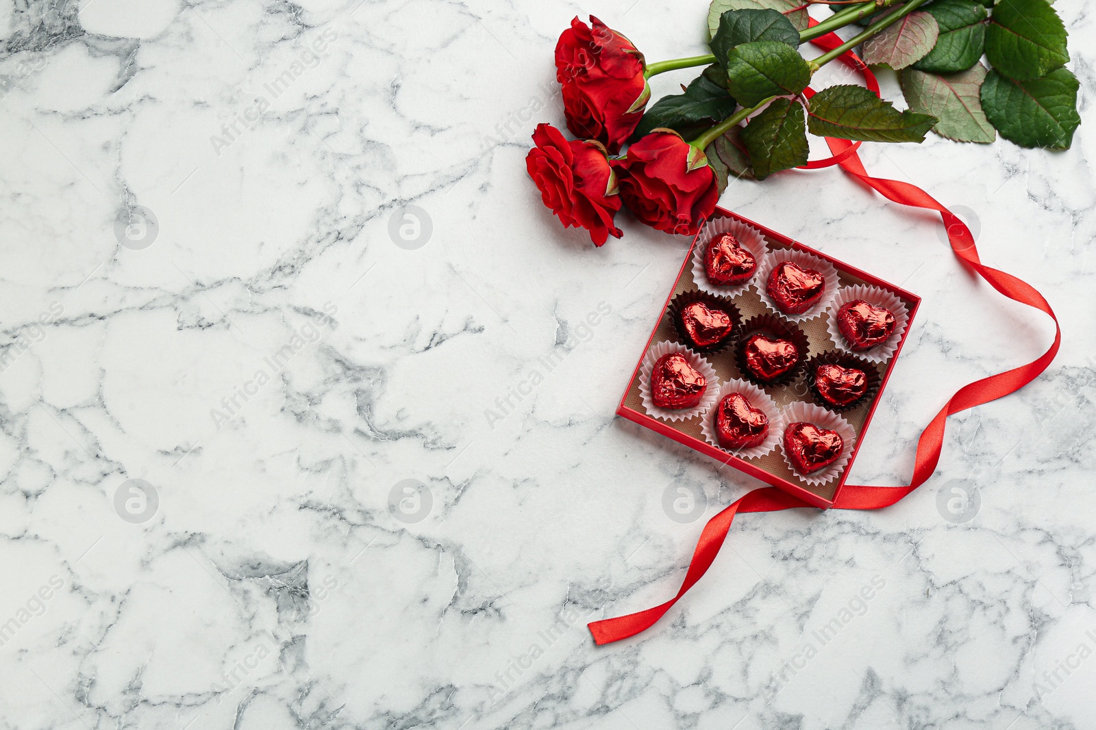 Photo of Heart shaped chocolate candies and bouquet on white marble table, flat lay. Space for text