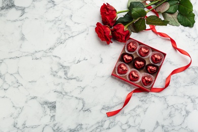 Photo of Heart shaped chocolate candies and bouquet on white marble table, flat lay. Space for text