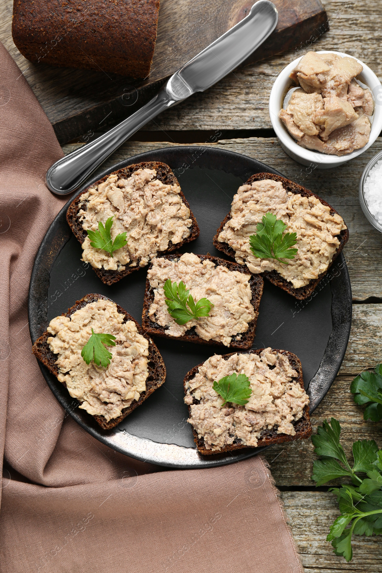 Photo of Tasty sandwiches with cod liver, salt and parsley on wooden table, flat lay