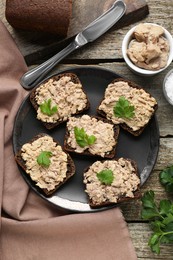 Photo of Tasty sandwiches with cod liver, salt and parsley on wooden table, flat lay