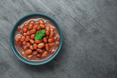 Photo of Bowl of canned kidney beans with parsley on grey table, top view. Space for text