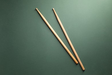 Two wooden drum sticks on olive background, top view