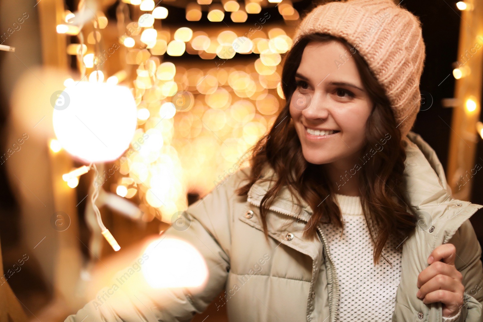 Photo of Beautiful young woman near festive lights outdoors. Winter vacation