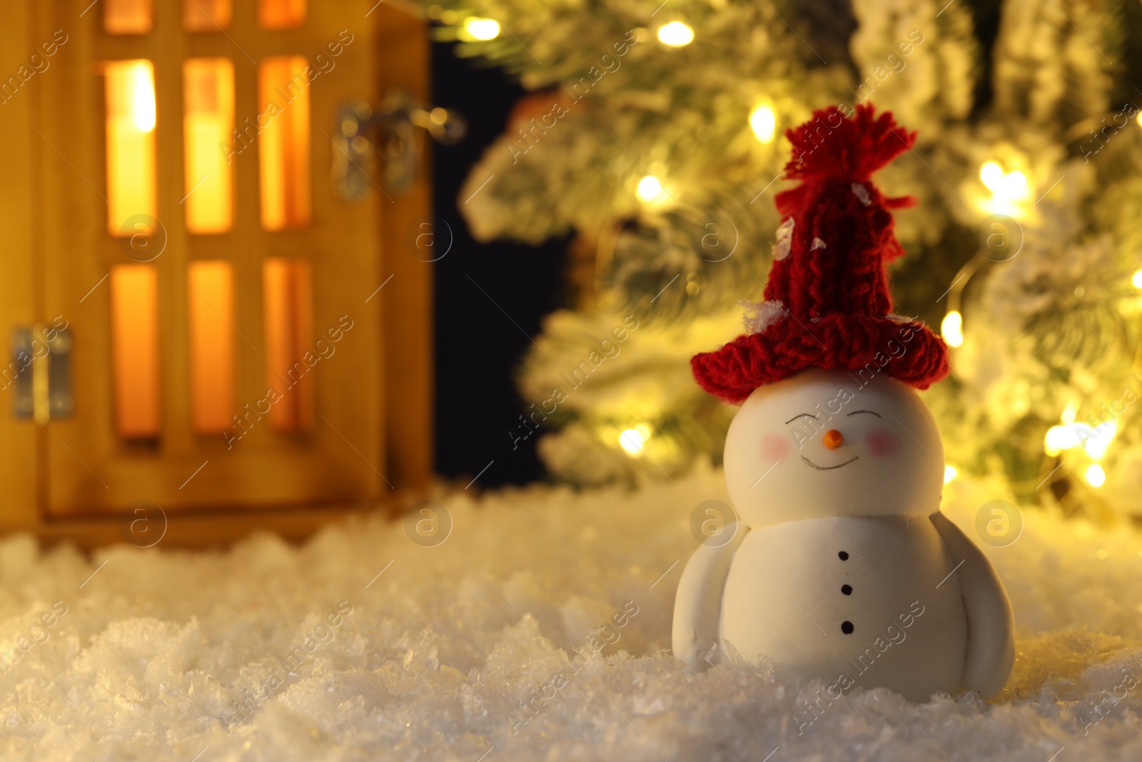Photo of Cute decorative snowman, lantern and Christmas tree on artificial snow
