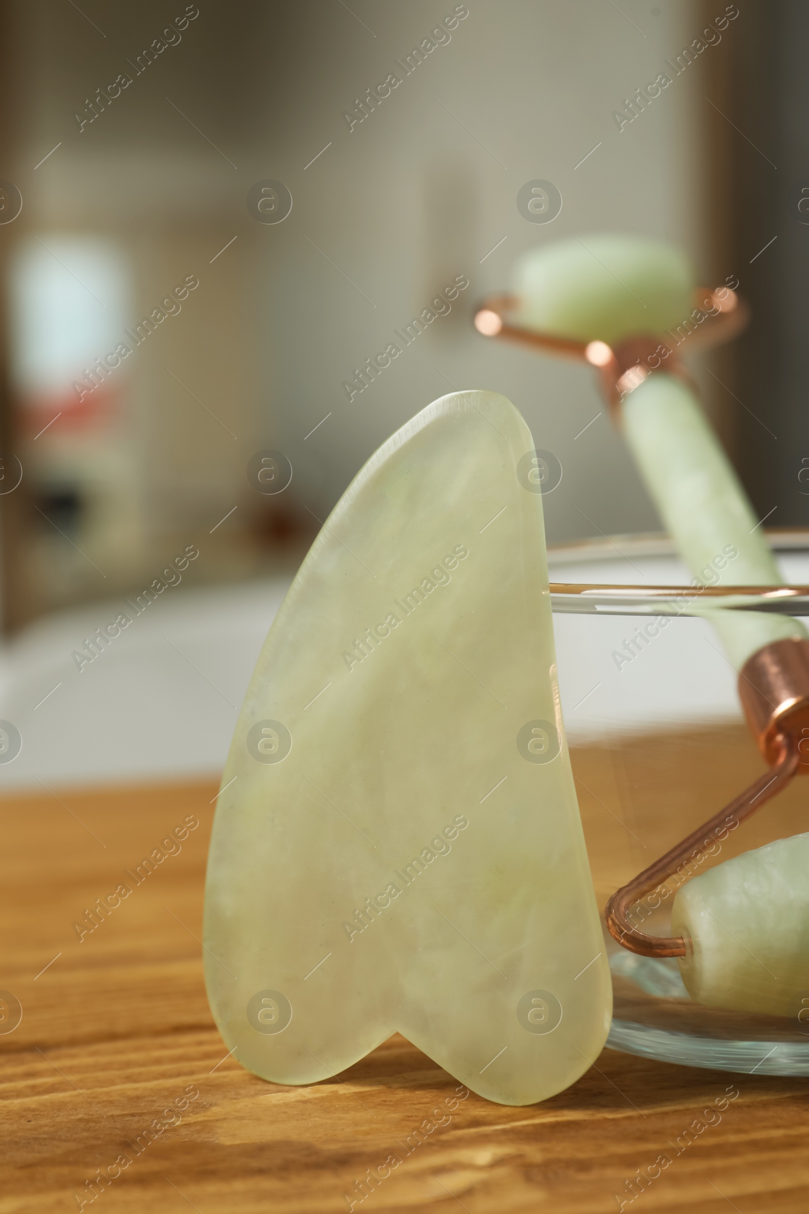 Photo of Jade gua sha tool and natural face roller on wooden bath caddy indoors, closeup