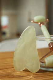 Photo of Jade gua sha tool and natural face roller on wooden bath caddy indoors, closeup