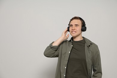 Photo of Handsome young man with headphones on light grey background. Space for text