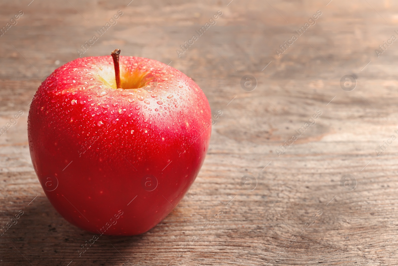 Photo of Ripe red apple with water drops on wooden background